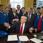 President Trump sits at the Resolute Desk surrounded by men in suits and two people in NASA jackets.