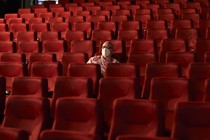 A man wearing a mask sits alone in a theater.