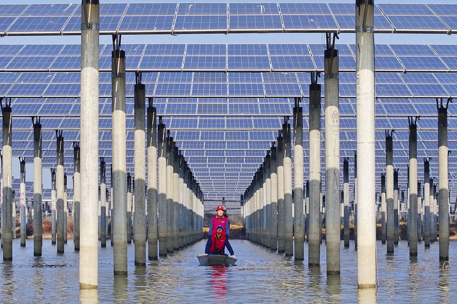 Three workers in a small boat check solar panels installed above a lake.