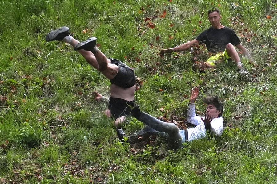 Three runners tumble down a steep grassy hill.