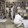 Men dressed in all white sit in a fluorescent room with bookshelves 