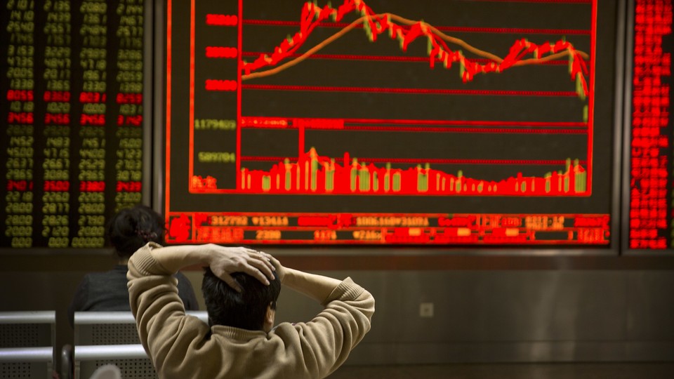 An investor holds his head in front of a red screen with fluctuating stock prices