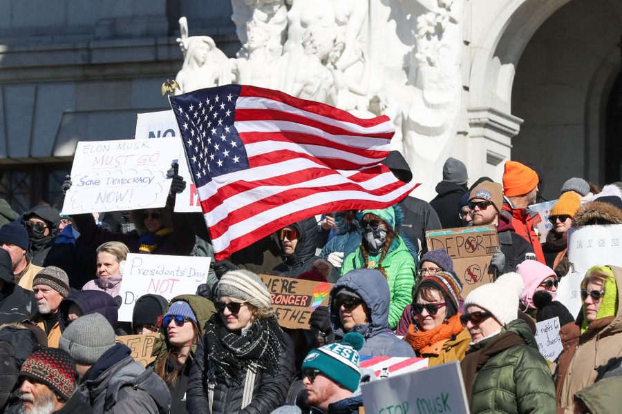 A group of protesters hold signs and an American flag.