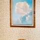 a cup in front of a painting of clouds against floral wallpaper