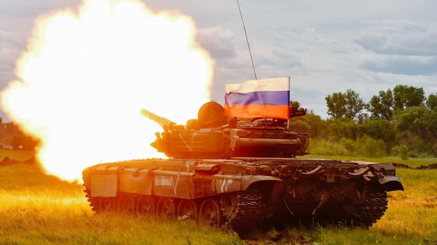 A Russian T-72 tank testfires with a Russian flag atop it.