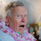 An older man wearing a pink lei surrounded by confetti