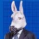 A businessman in a suit is shown wearing a donkey mask.