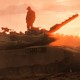 A man standing on top of a tank as the sun sets