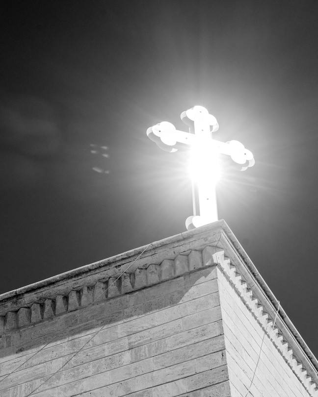 A cross on a rooftop, the sun illuminating it from behind