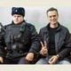 A photo of Alexei Navalny flashing a V sign with his fingers next to a guard