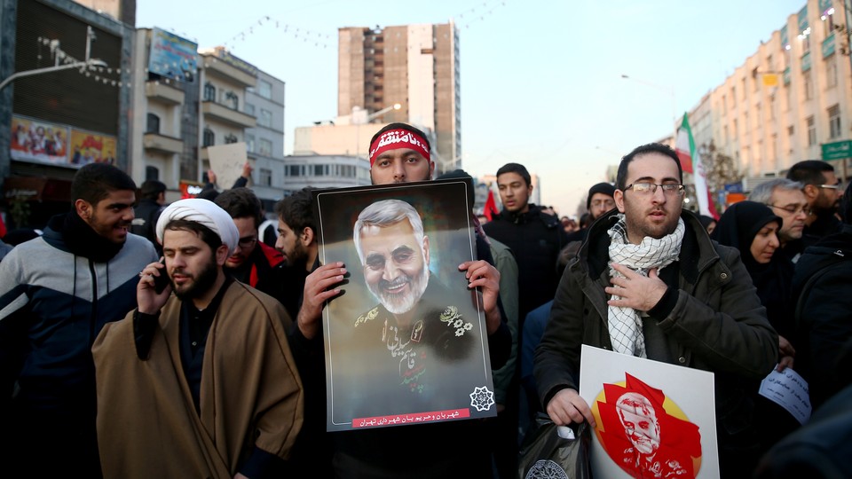 A man holds a photograph of Qassem Soleimani during the general's funeral procession while walking next to others.