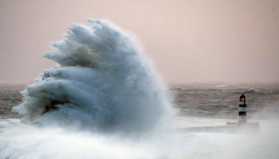 A large wave splashes against a pier.