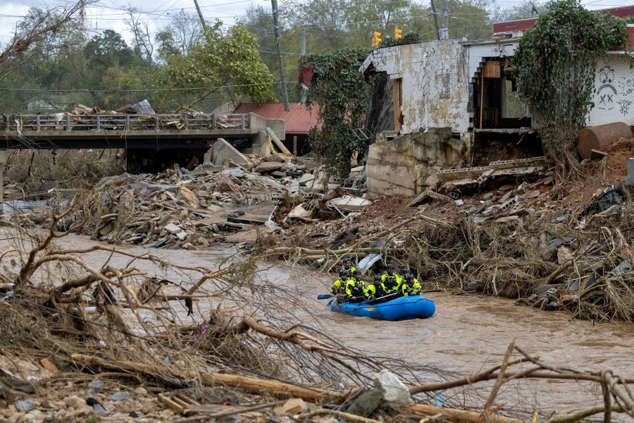 A rescue team paddles down a river past piles of flood debris.