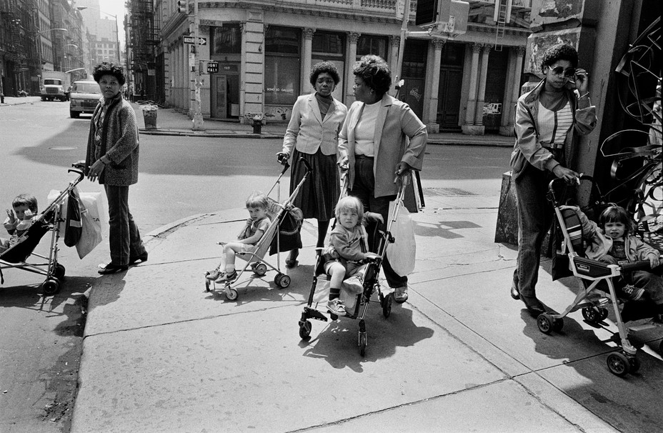 Black women with strollers of white children at a corner.