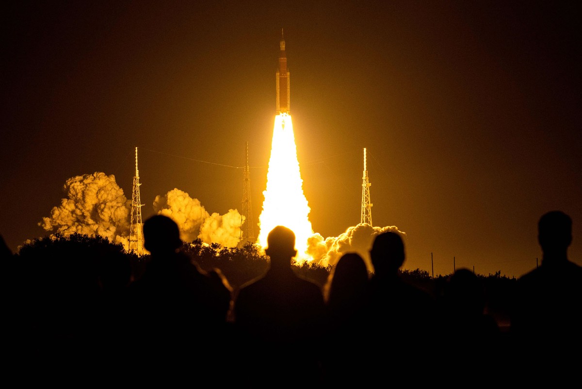 People watch as a large rocket blasts off at night.