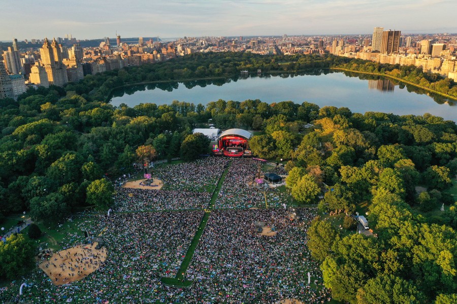 An aerial view of thousands of attendees watching a live event in a park.