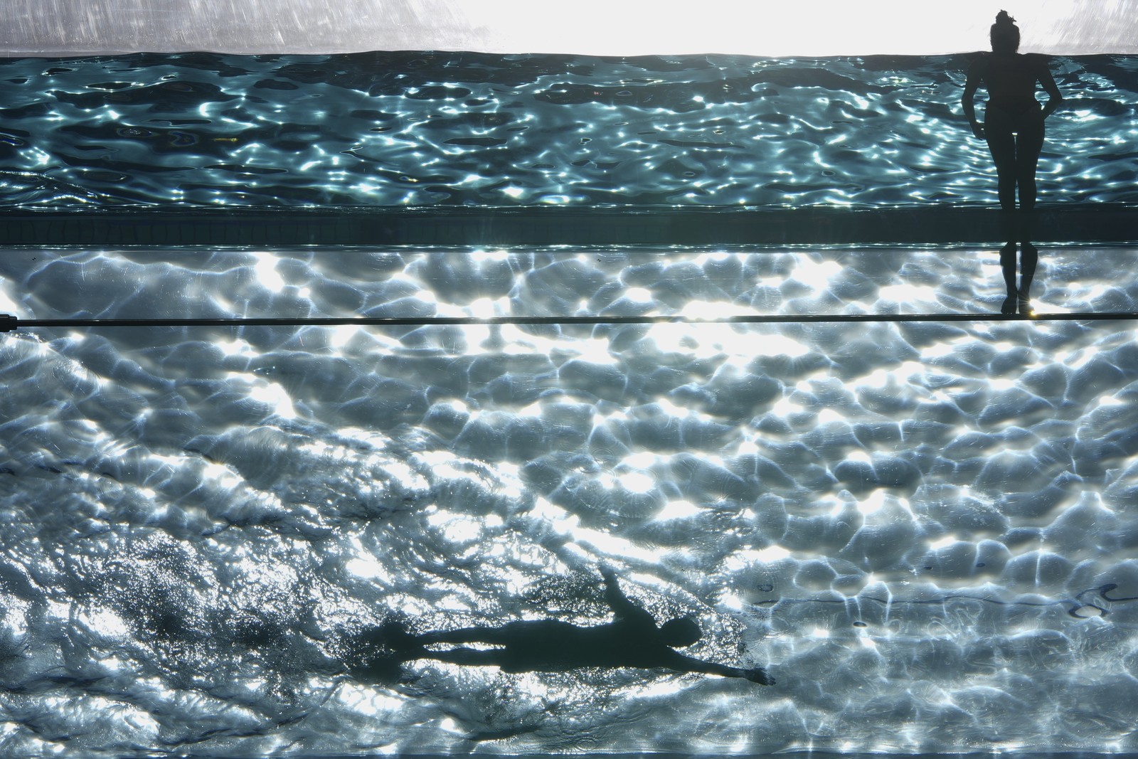 A view from beneath of two swimmers in a clear-bottomed swimming pool.