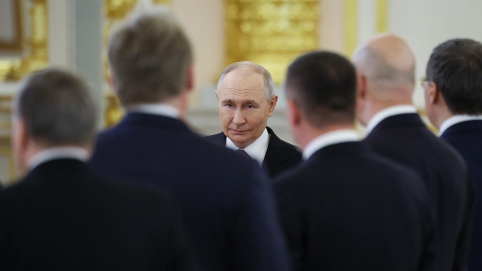 Several men in suits stand with their backs to the camera while Putin faces it head-on, in sharp focus
