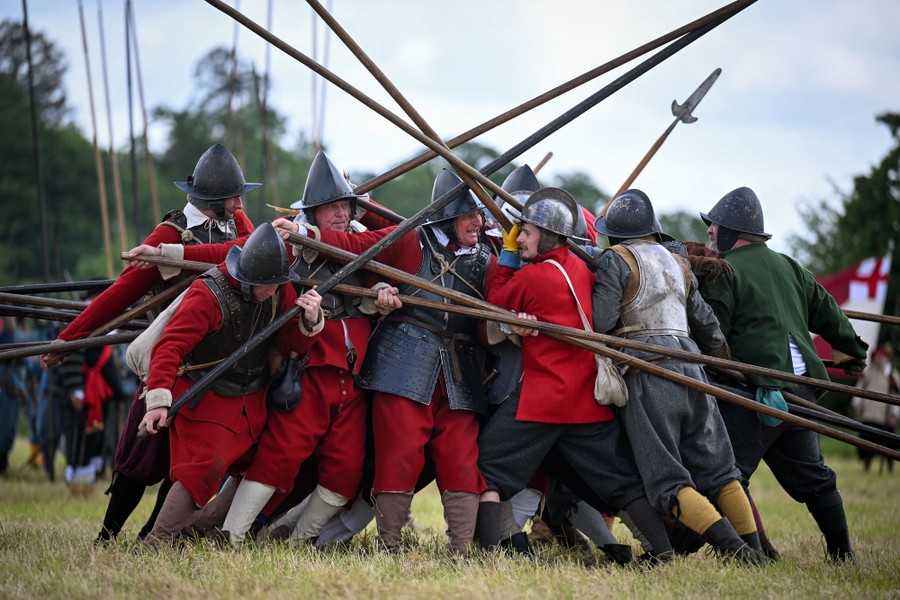 People wearing 17th-century uniforms and helmets re-create a battle using long pikes.