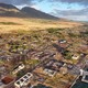 An aerial view of a small Hawaiian town, made up mostly of destroyed buildings and empty plots, one year after a wildfire