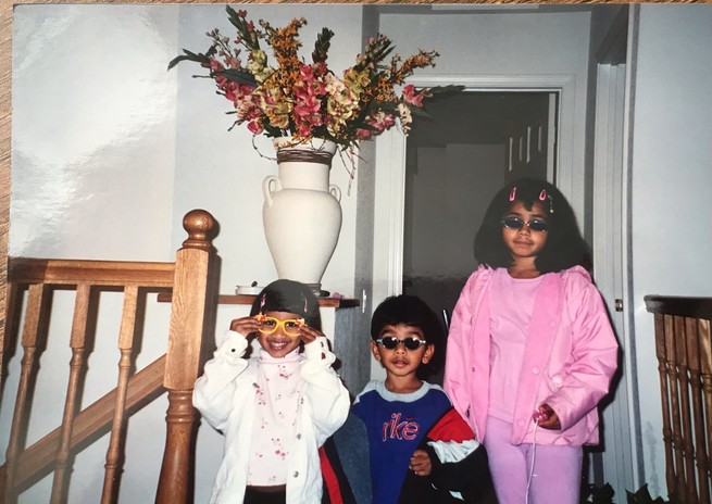 Two young kids and one preteen stand in a foyer wearing sunglasses and sweatshirts