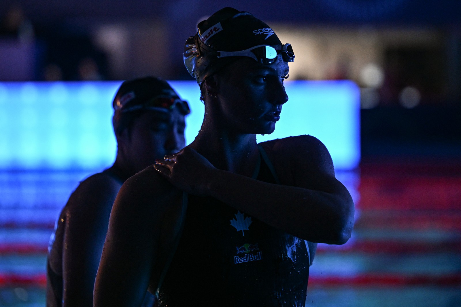 Two swimmers stand near a pool, after a race.