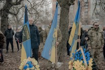 Ukrainian military men and civilians holding Ukrainian flags in a cemetery