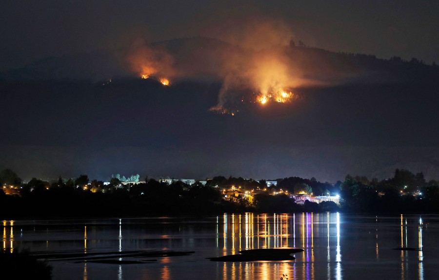A view of a forest fire burning on a hillside above a small town.