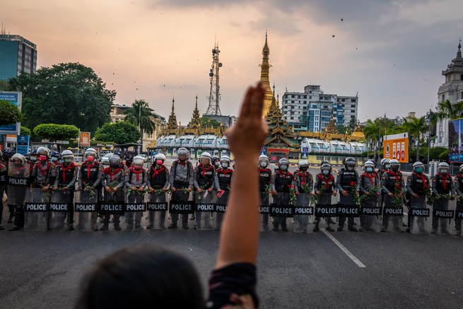 A protester makes a three-finger salute in front of a row of riot police, who are holding roses given to them by protesters in Yangon, Myanmar.
