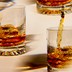 photo of brown liquor being poured over ice into multiple highball glasses