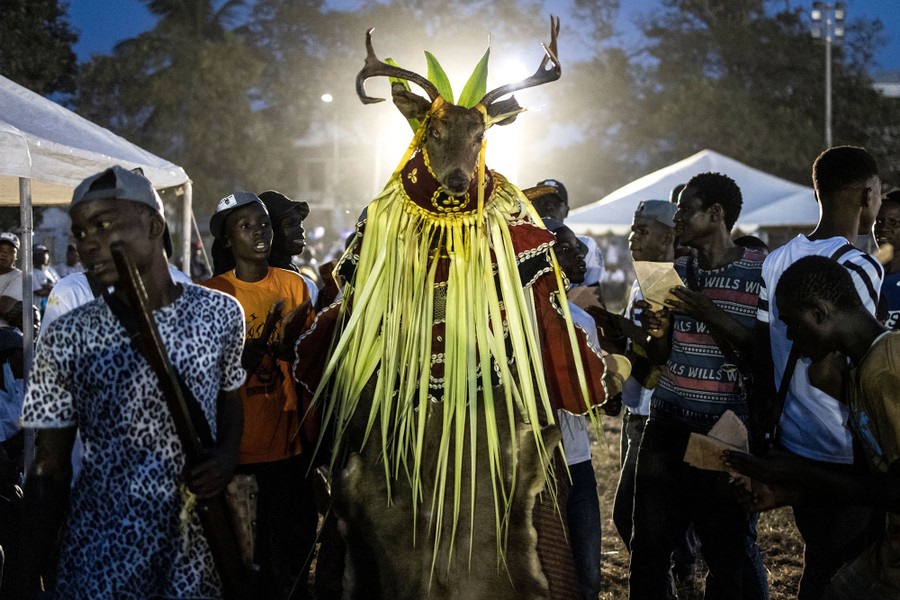 Several people gather at a rally; one wears a traditional costume topped with a deer mask.