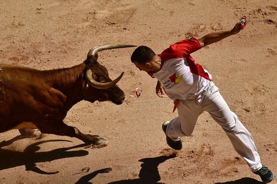 A man looks over his shoulder while dodging a bull running toward him.