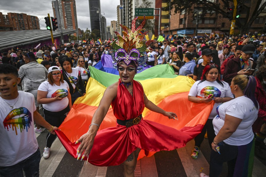 People march in a Pride parade, including one in a gown with a long rainbow-colored train.