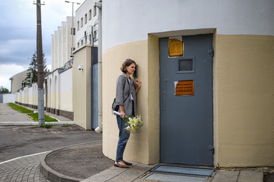 A woman with a bouquet of flowers waits beside the outer door of a detention center.