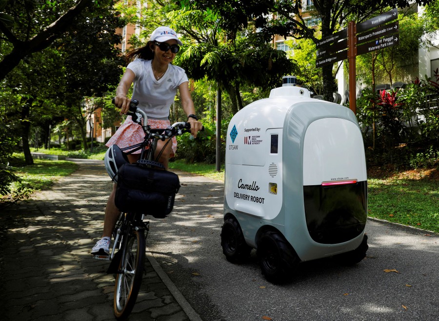 A person rides their bike past a small four-wheeled robot on a sidewalk.