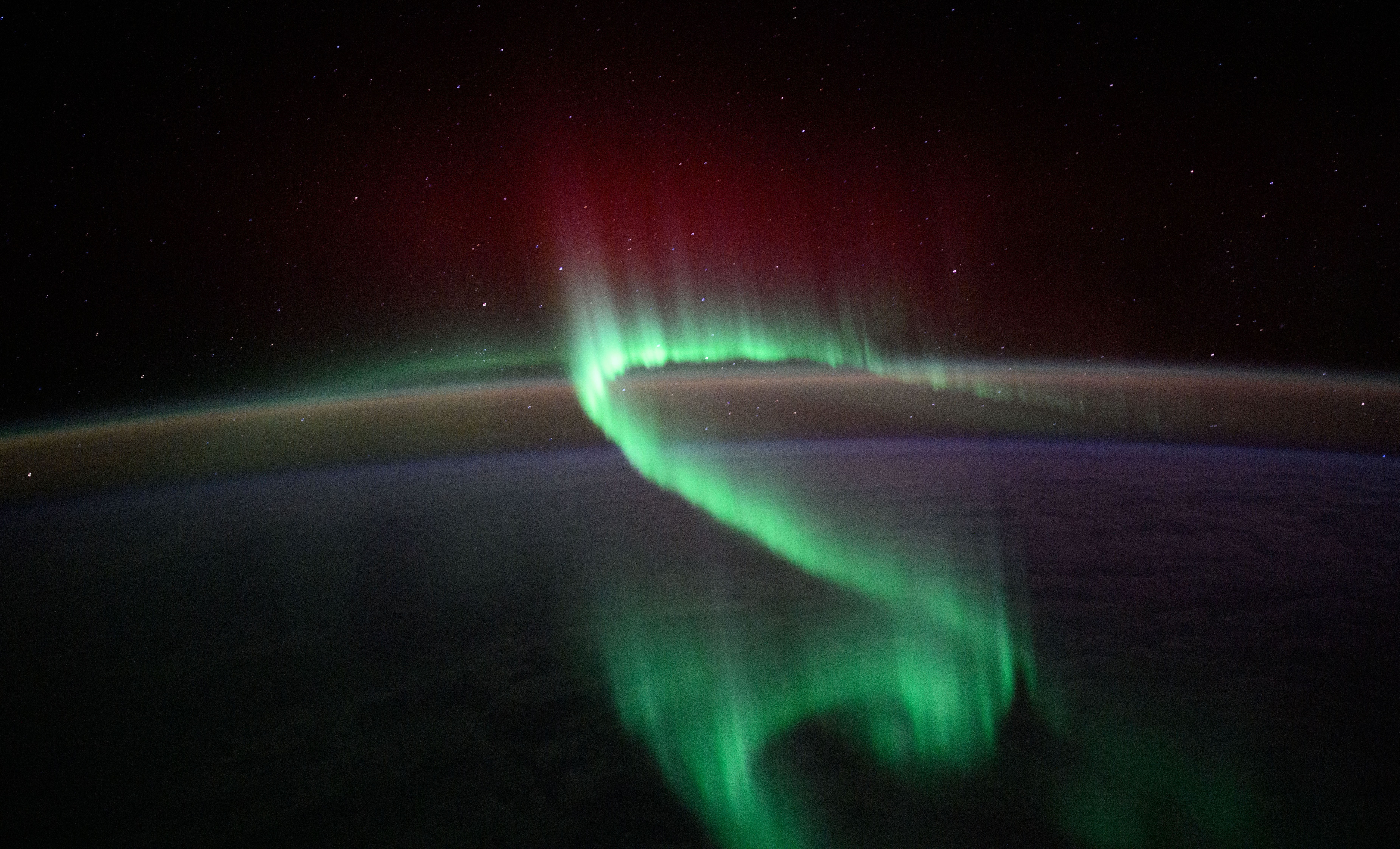 A green ribbon-like aurora lights up the sky, seen from orbit.