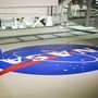 A person lies on a surface while painting a large NASA logo.