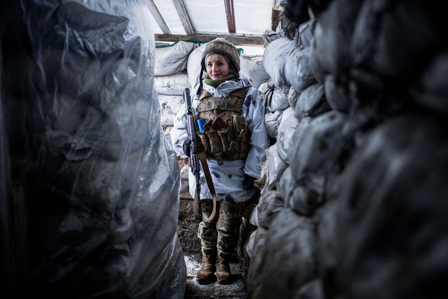 A soldier stands in a narrow trench surrounded by sandbags.