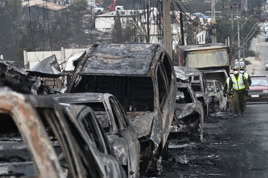 Several law-enforcement officers walk past a row of burned cars.