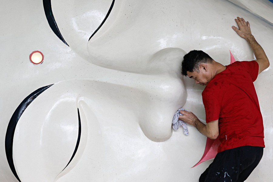 A man cleans the nose of a large sleeping Buddha statue.