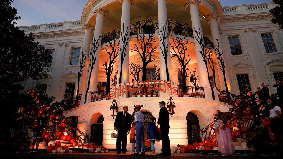 Trump passes out candy in front of a halloween-decorated White House.