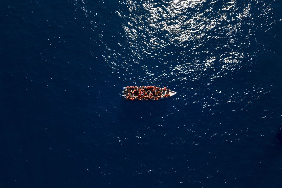 An aerial view of more than a dozen people in a small boat, wearing life preservers