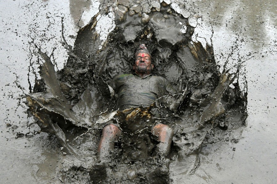 A person falls backwards, splashing into a muddy ride paddy.
