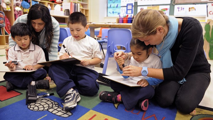 Preschool children sit and read with adults on a colorful rug.