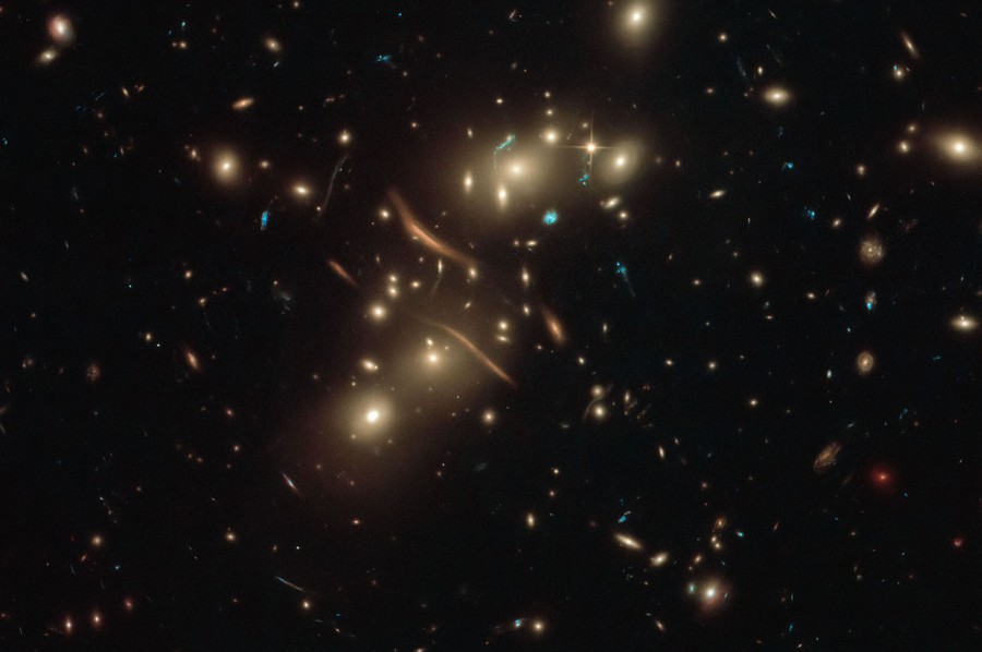 Dozens of distant galaxies are seen, with several twisted and smeared streaks of light at center.