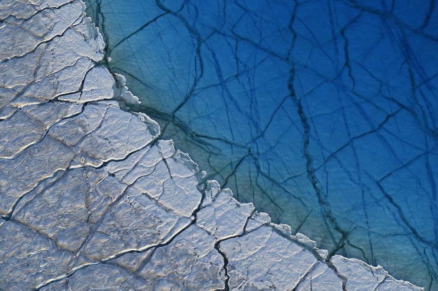 An aerial view of a meltwater lake on an ice cap, with many cracks