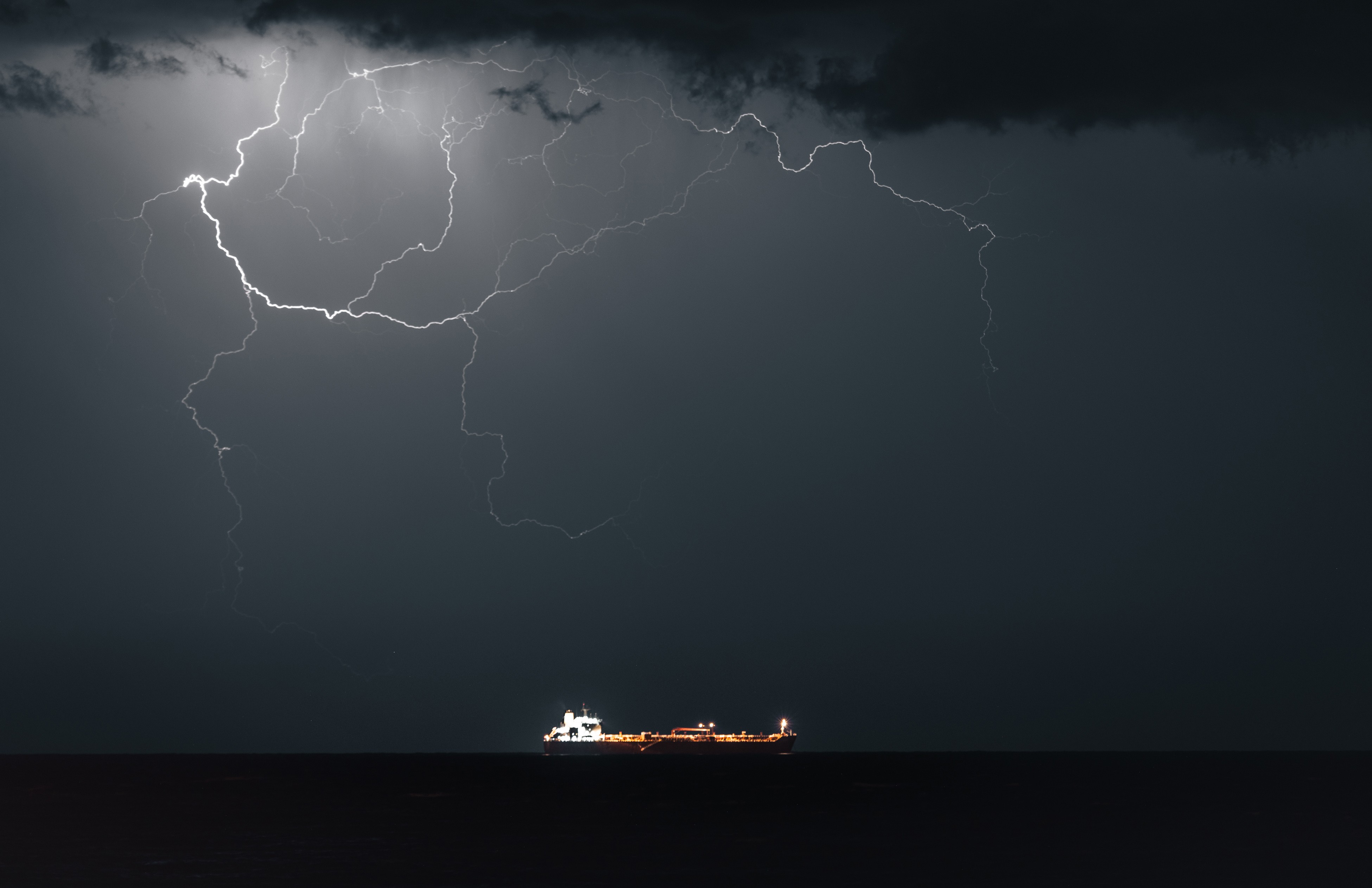 Lightning strikes in the night sky above an oil tanker.