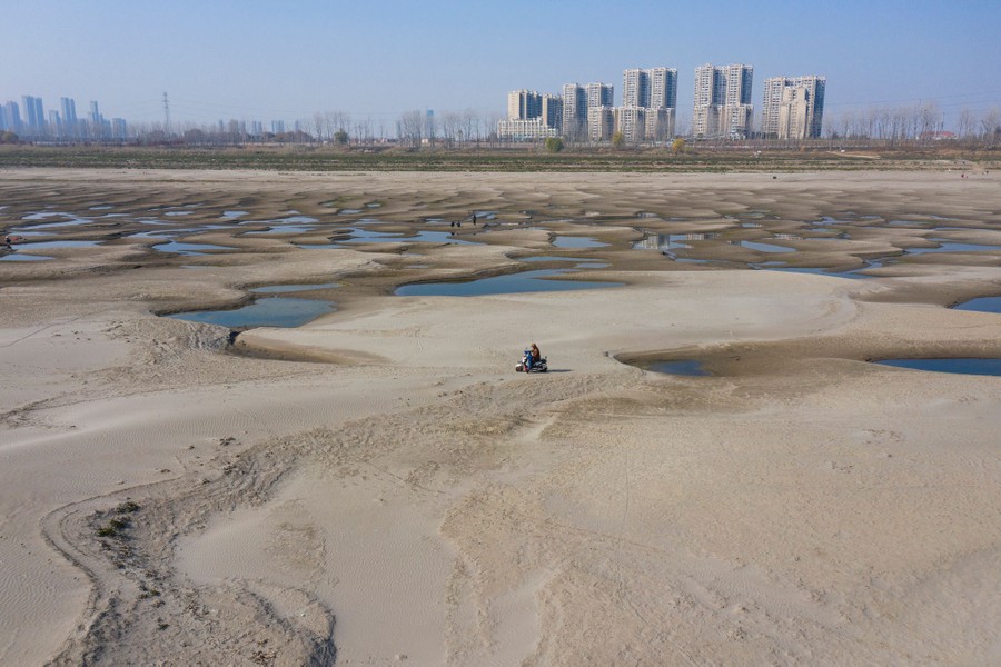 A person rides a scooter on the broad sandy bottom of a dry river.