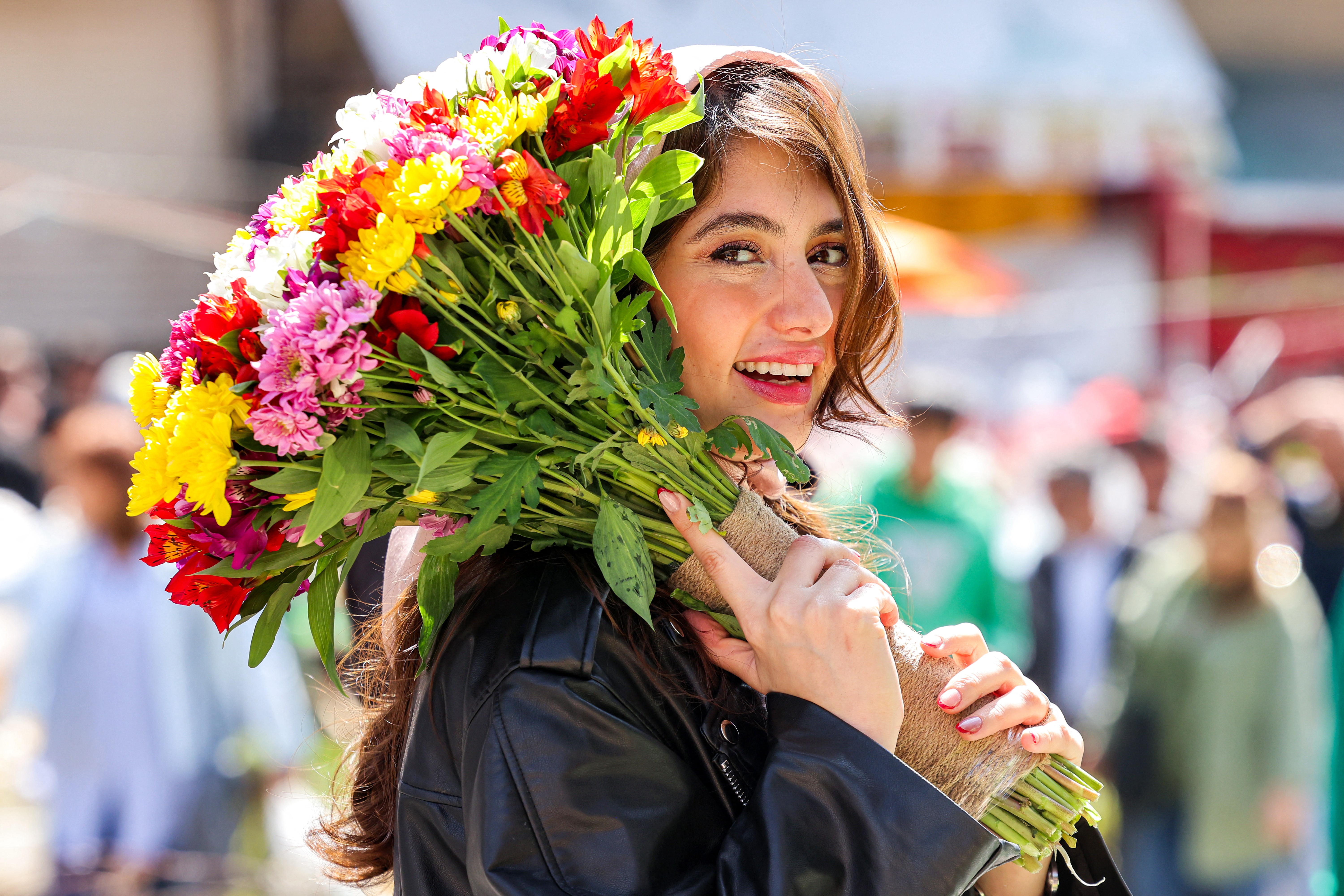 A woman smiles while holding a bouquet of flowers in an open market.