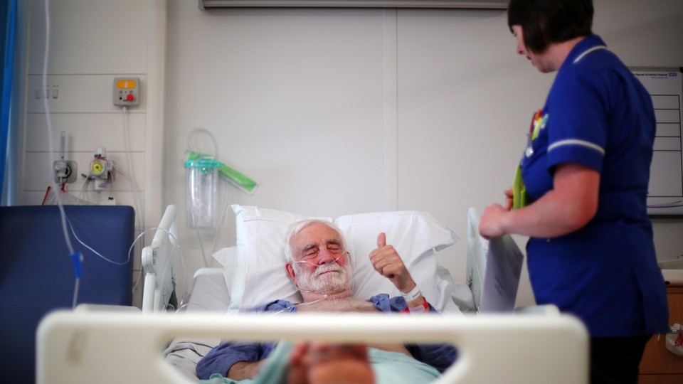 A man giving the "thumbs-up" sign in a British hospital bed